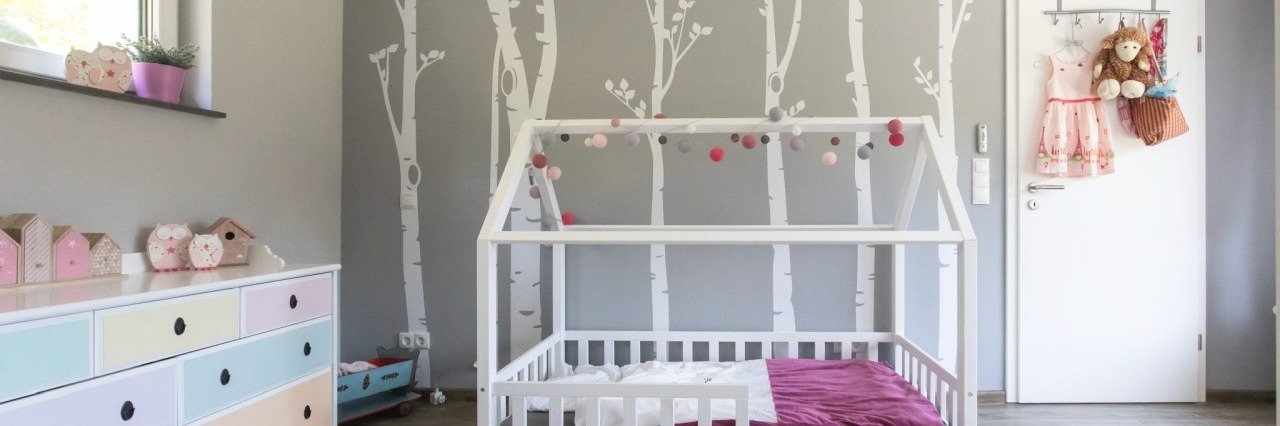 Modern gestaltetes Kinderzimmer mit hellgrauer Akzentwand, Birkenstamm-Wanddesign und bunten Möbeln – realisiert mit hochwertigen Innenwandfarben von Farbdepot Weber GmbH.